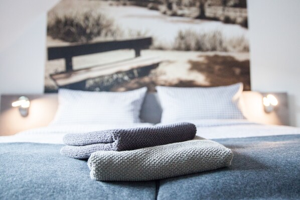 A neatly made bed with a blanket and pillows, a painting of a landscape on the wall behind, and a bedside lamp. - Pension Dalinghaus (Neuenkirchen-Vörden)