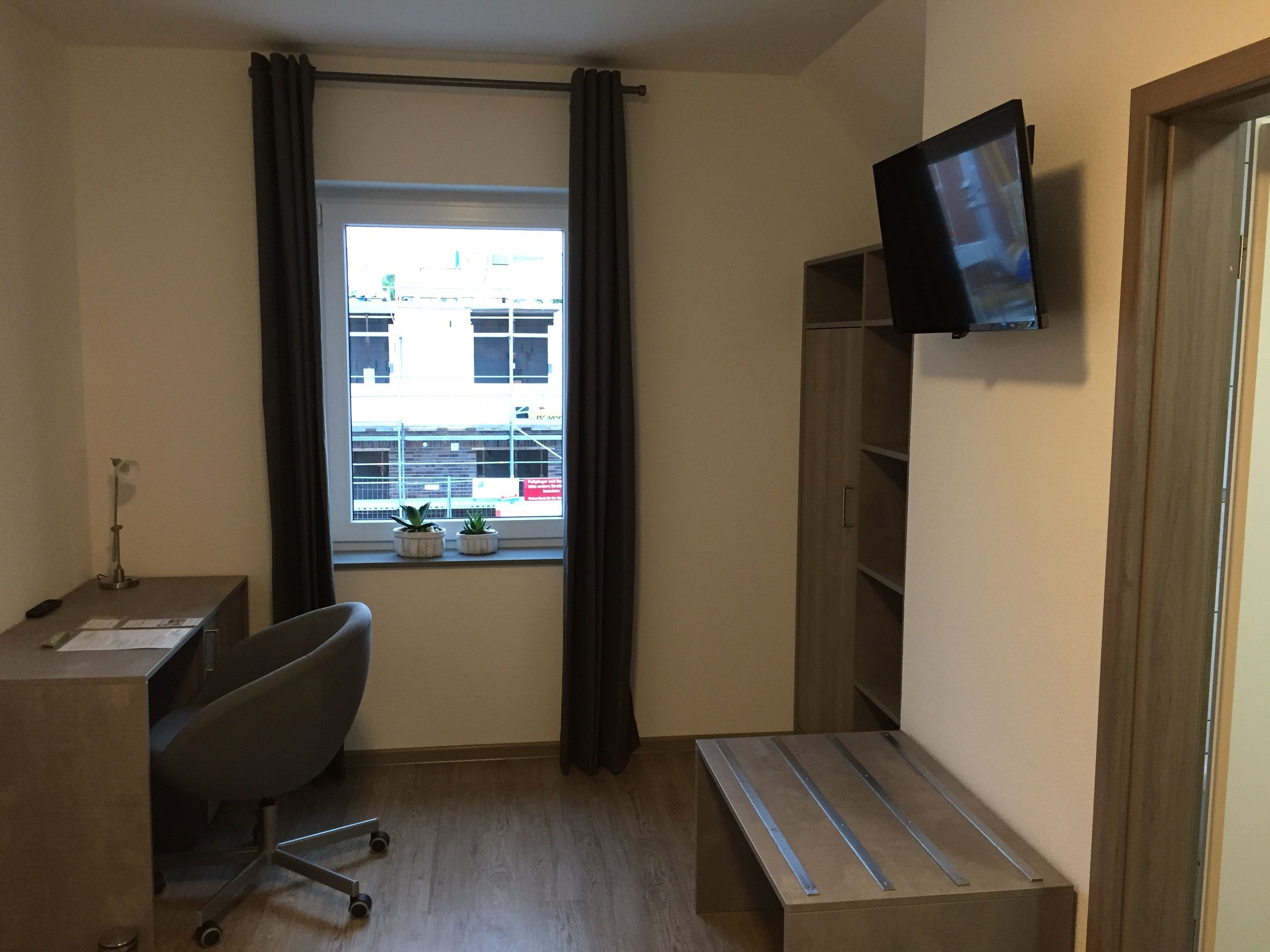Ein kleiner, zweckmäßiger Arbeitsraum mit Schreibtisch, Stuhl und an der Wand befestigtem Fernseher.