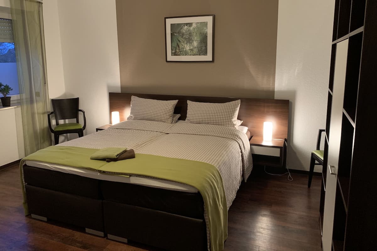 Een slaapkamer met een bed, een stoel, een nachtkastje en een aan de muur bevestigd schilderij.