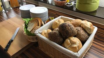 A breakfast buffet with various breads, a knife on a cutting board, and a glass of orange juice.