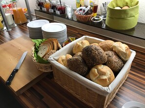 A breakfast buffet with various breads, a knife on a cutting board, and a glass of orange juice. - Pension Dalinghaus (Neuenkirchen-Vörden)