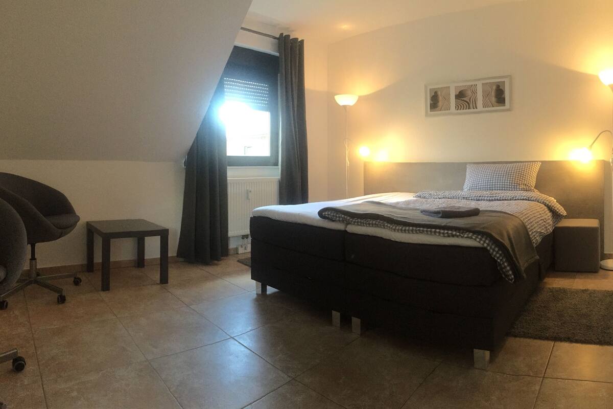 Een slaapkamer met een bed, twee stoelen, een klein tafeltje en twee bedlampjes.