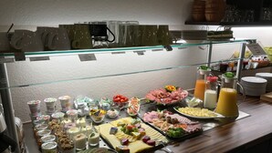 Een buffet met diverse gerechten, waaronder fruit, kazen en vlees, gepresenteerd op een toonbank met een glazen afscheiding.