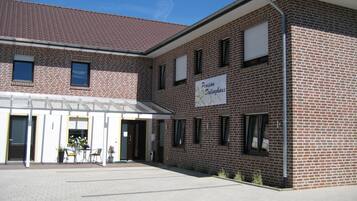 A brick building with a sign reading "Pension Dalinghaus" and a covered entrance area with chairs and potted plants.