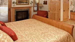 A bedroom with a large bed, a fireplace, wooden doors, and a red chair. - Vail Residences at Hotel Talisa (Vail)