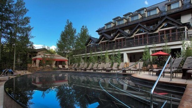 A swimming pool with a glass bottom, surrounded by lounge chairs and a building with balconies. - Vail Residences at Hotel Talisa (Vail)