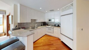A modern kitchen with white cabinetry, granite countertops, a built-in oven, microwave, and a stainless steel sink. - Vail Residences at Hotel Talisa (Vail)