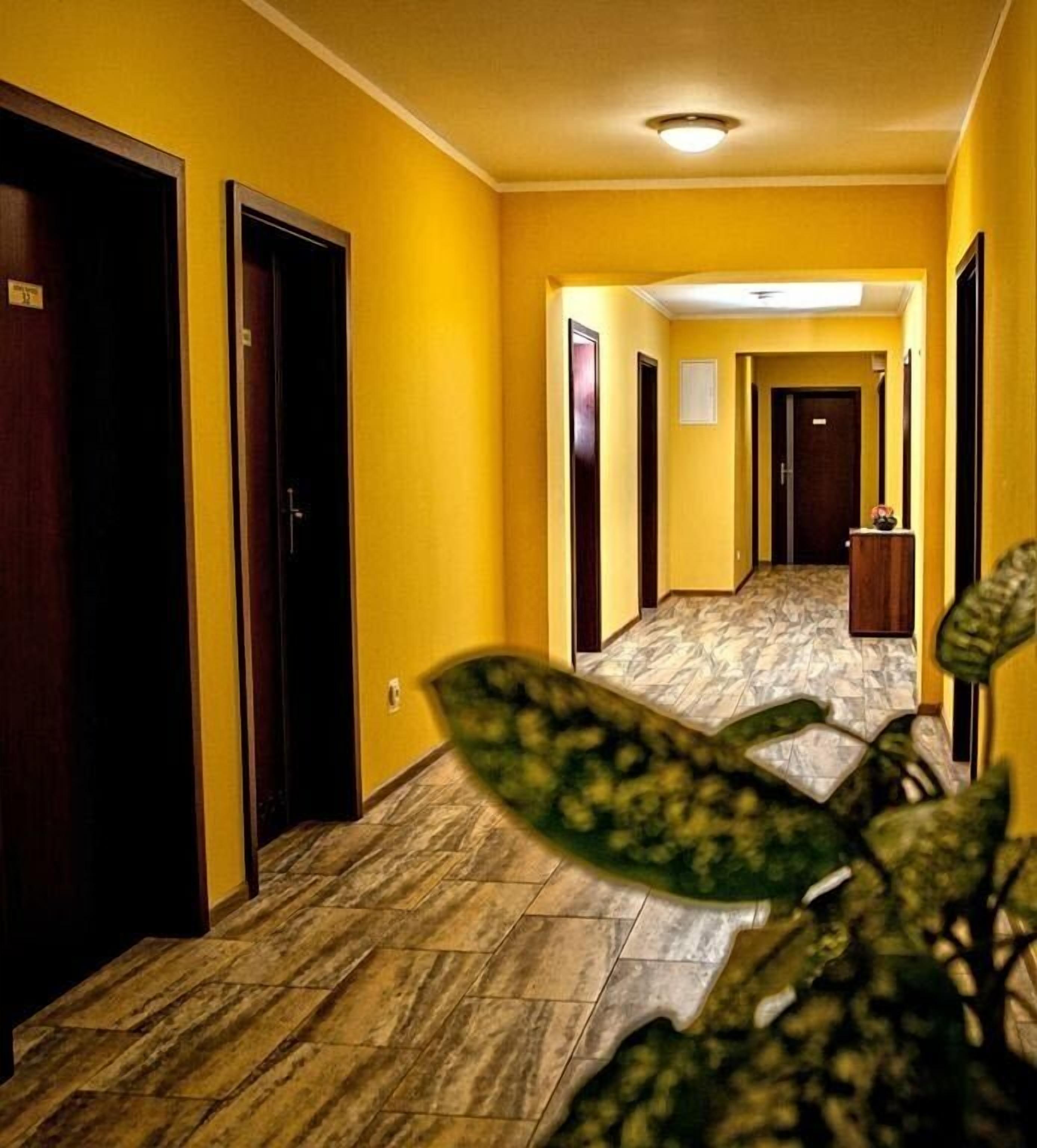 A hotel hallway with yellow walls, wooden doors, and a marble floor.
