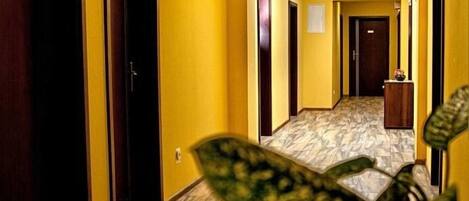 A hotel hallway with yellow walls, wooden doors, and a marble floor.