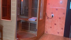 A sauna room with a wooden bench, a glass door, and a red rug on the floor. - Hostel mPark Myslowice (Myslowice)