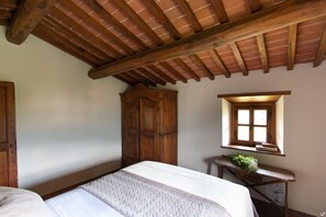 Un dormitorio con techo de madera, un armario grande, una mesita con una planta y una ventana con persianas.