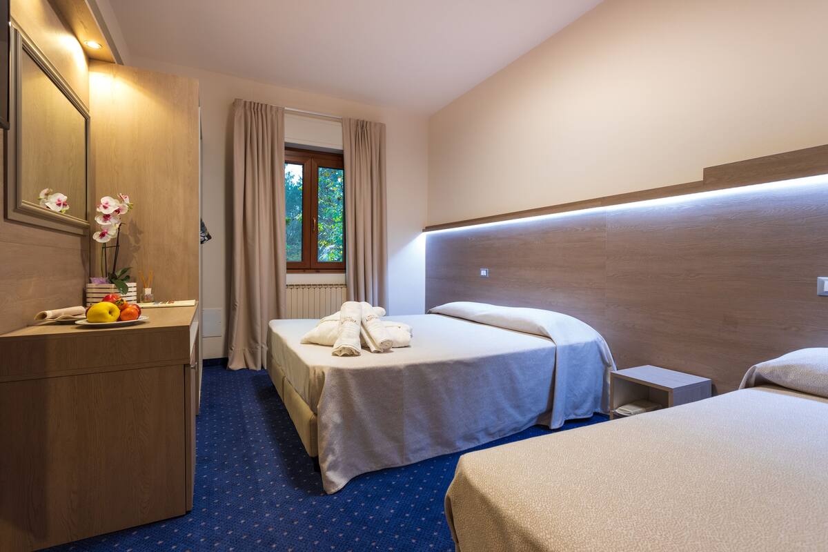 A hotel room with a bed, a bedside table, a dresser, a mirror, and a window with curtains.