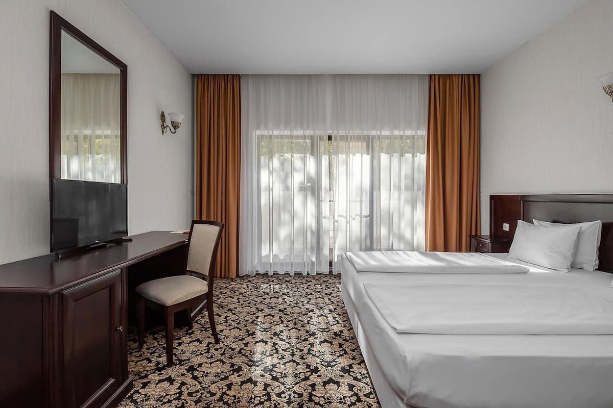 Une chambre d’hôtel comprenant un lit, un bureau avec une chaise, une télévision et une grande fenêtre avec des rideaux.