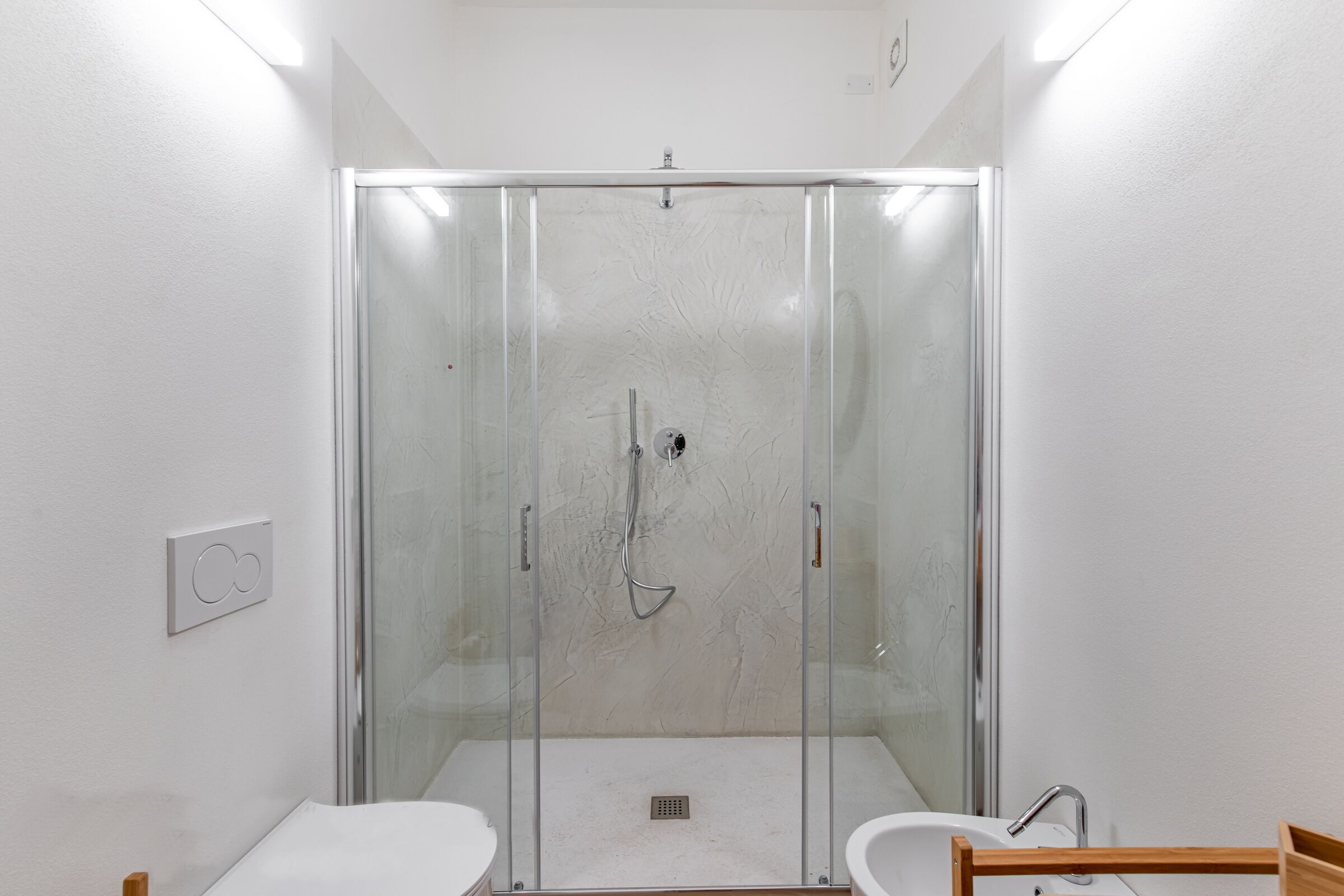 A modern bathroom with a glass-enclosed shower, a white sink, and a wooden bench.