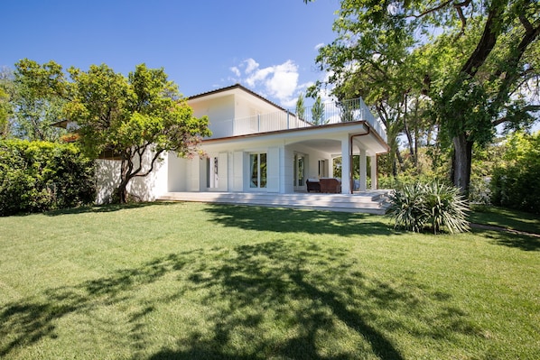 A modern two-story house with a covered porch, surrounded by a well-maintained lawn and trees.