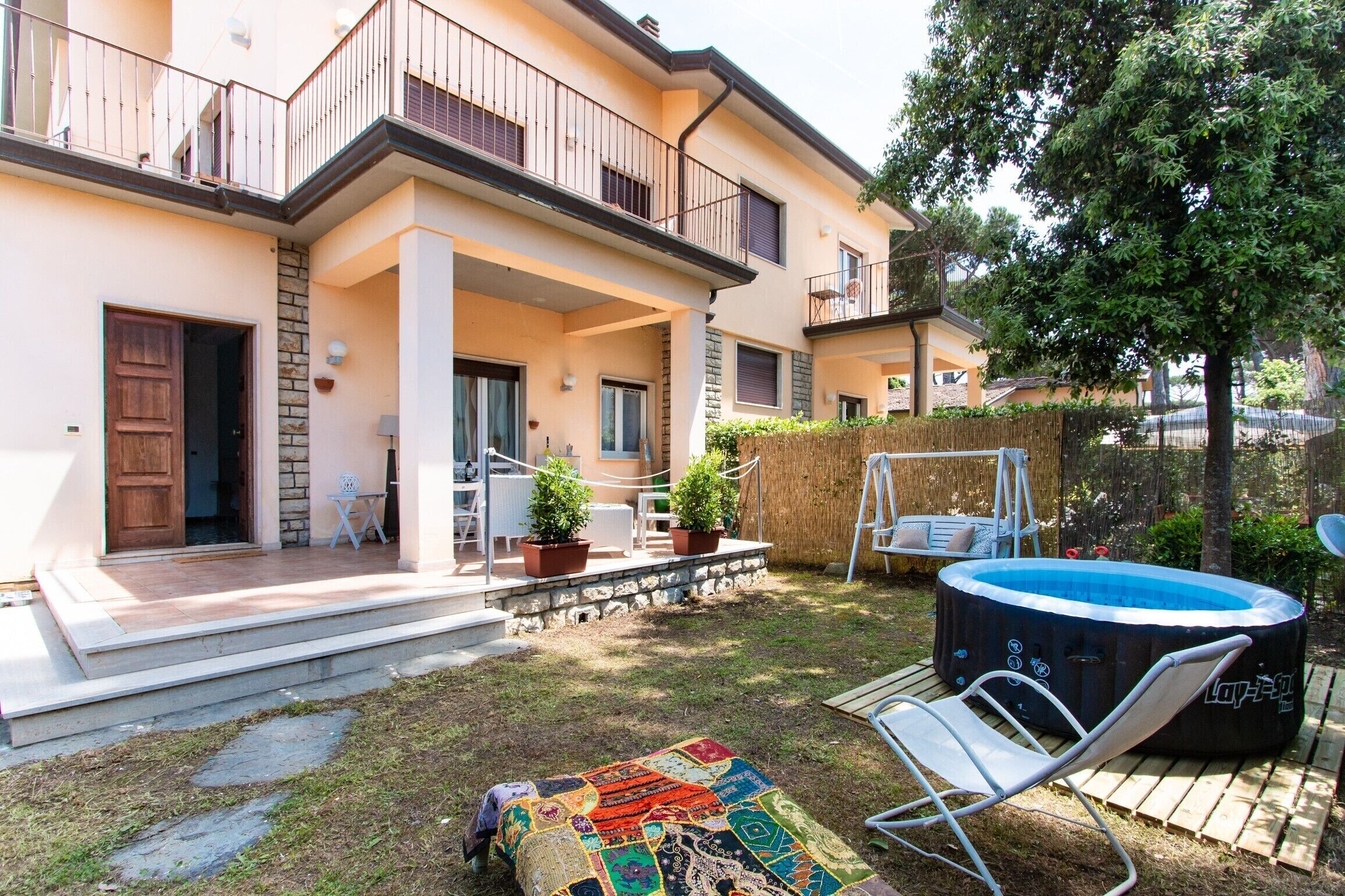 A two-story residential building with a balcony, a hot tub, and a garden area with a swing set.