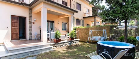 A two-story residential building with a balcony, a hot tub, and a garden area with a swing set.