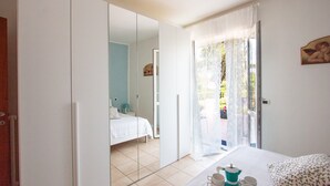 A bedroom with a bed, a bedside table, a mirror, and a window with curtains. - Villa Franca (Pietrasanta)
