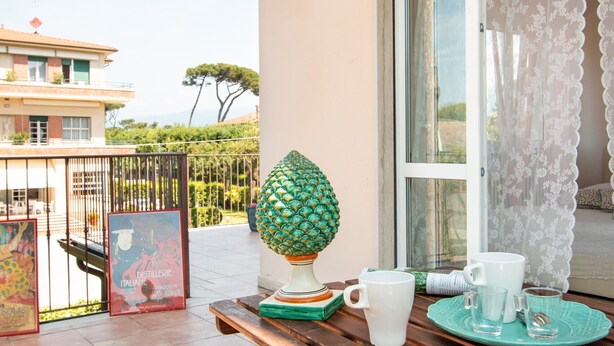 A balcony with a decorative lamp, a table with a white mug and glasses, and a poster. - Villa Franca (Pietrasanta)