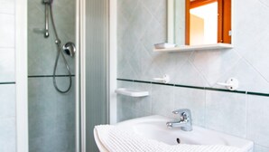 A modern bathroom with a glass shower enclosure, a white sink with a towel, and a mirror above the sink. - Villa Franca (Pietrasanta)