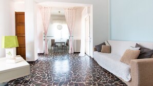 A living room with a sofa, a coffee table, and a lamp. There is a dining area in the background with a table and chairs. - Villa Franca (Pietrasanta)