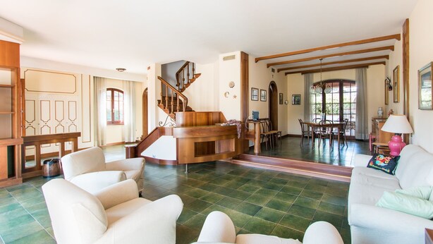 A spacious living area with a wooden staircase, a dining area, and a reception desk. - Villa Gloria (Pietrasanta)