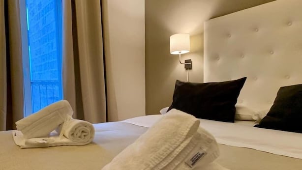 A hotel room with a neatly made bed, a wall-mounted lamp, and a window with curtains. - A Due Passi dal Ponte (Taranto)