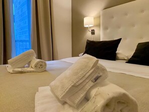 Quarto de hotel com cama bem arrumada, luminária na parede e janela com cortinas.