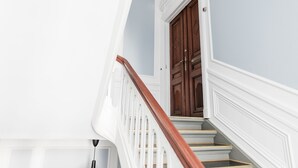 Eine Treppe mit weißen Geländern und Holzstufen, die zu einer dunklen Holztür führt.