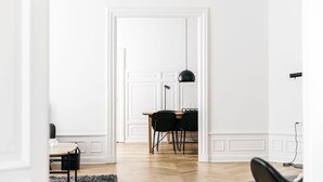Ein modernes, minimalistisches Zimmer mit Holzboden, weißen Wänden und einem Essbereich mit Tisch und Stühlen.