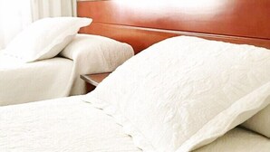 Una habitación de hotel con cabecera de madera, dos camas individuales con ropa blanca y una mesita de noche.