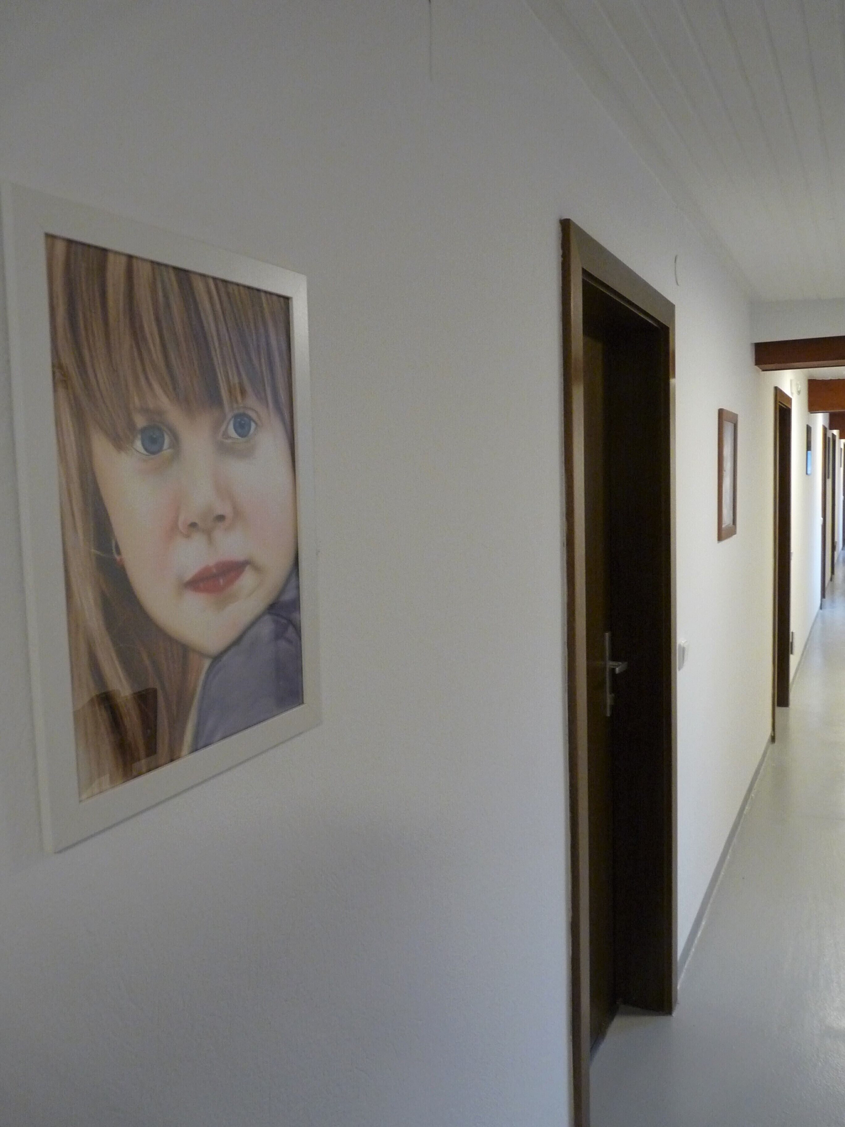 Ein Flur mit gerahmten Bildern an den Wänden, Holztüren und einer weißen Decke.