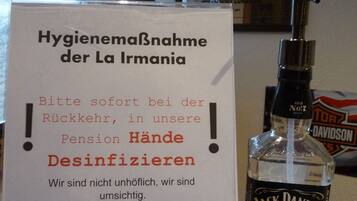 Ein Schild in deutscher Sprache zu Hygienemaßnahmen, eine Flasche Jack Daniel's Whiskey und ein gerahmtes Bild an der Wand.