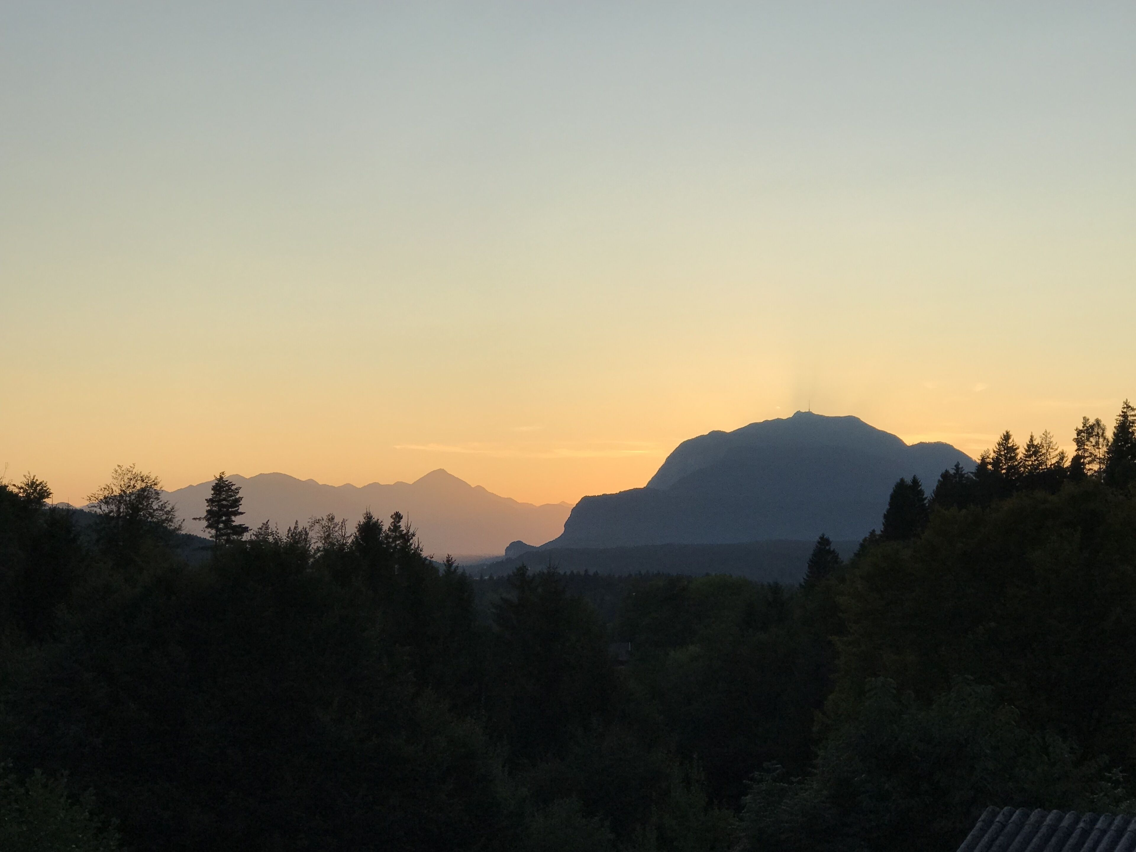 A mountain landscape at sunset with a silhouette of a mountain and trees in the foreground.