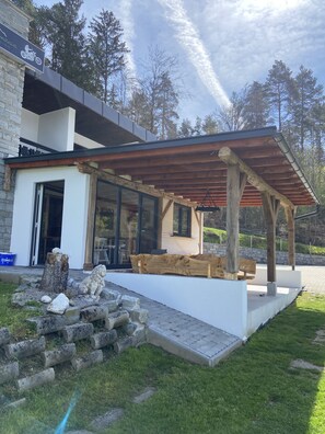 Un patio exterior moderno con una pérgola de madera, escalones de piedra y un banco de piedra.