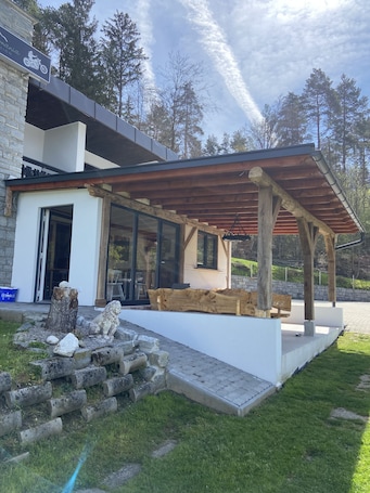 A modern outdoor patio area with a wooden pergola, stone steps, and a stone bench.