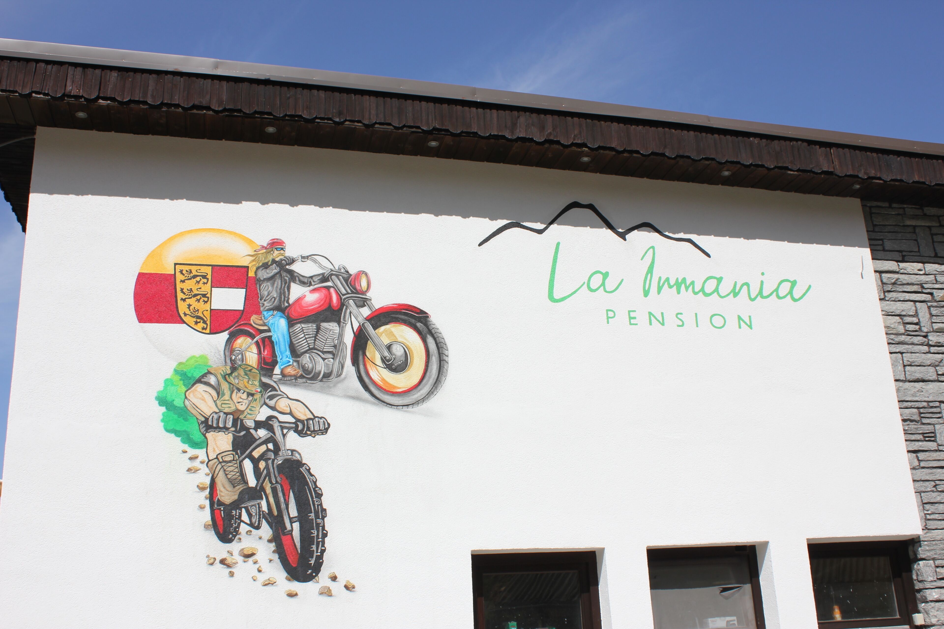 A building with a mural of a motorcycle and a shield, and the text "La Irmania Pension".