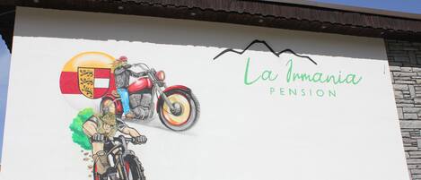 Un bâtiment orné d’une fresque représentant une moto et un blason, ainsi que de l’inscription « La Irmania Pension ».