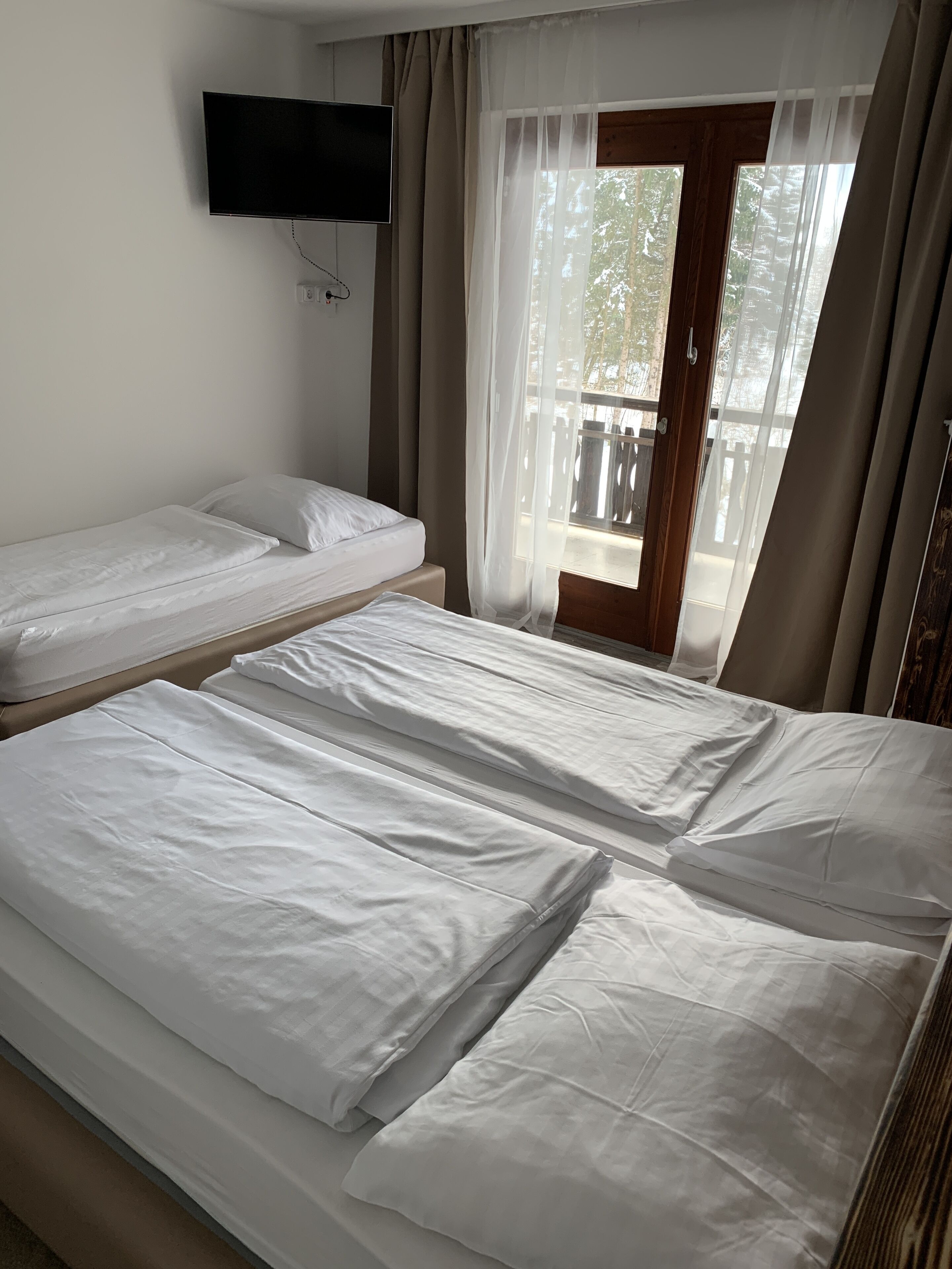 A hotel room with two single beds, a television mounted on the wall, and a balcony with a wooden railing.