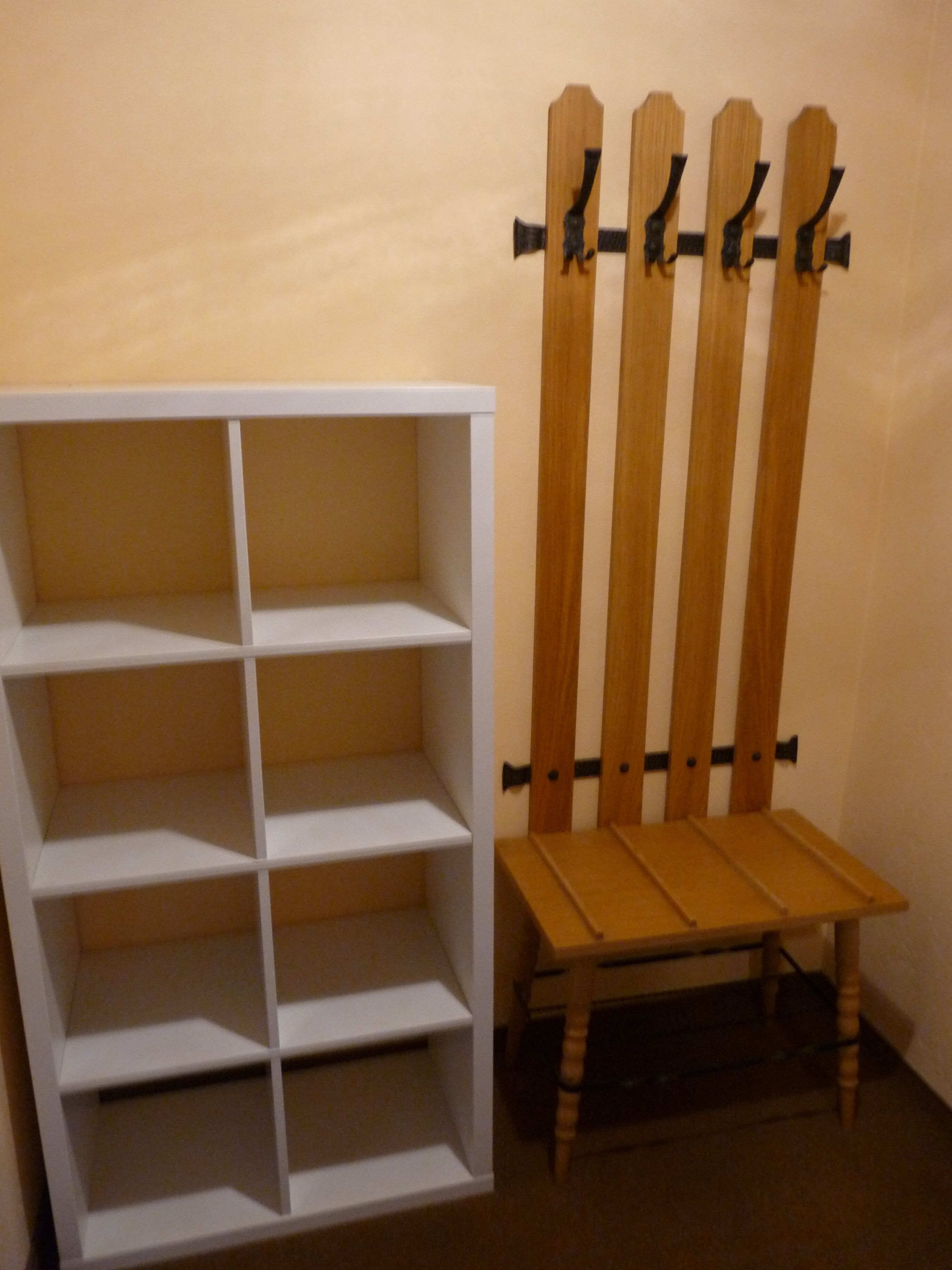 A white shelving unit with multiple compartments and a wooden chair with a backrest against a wall.