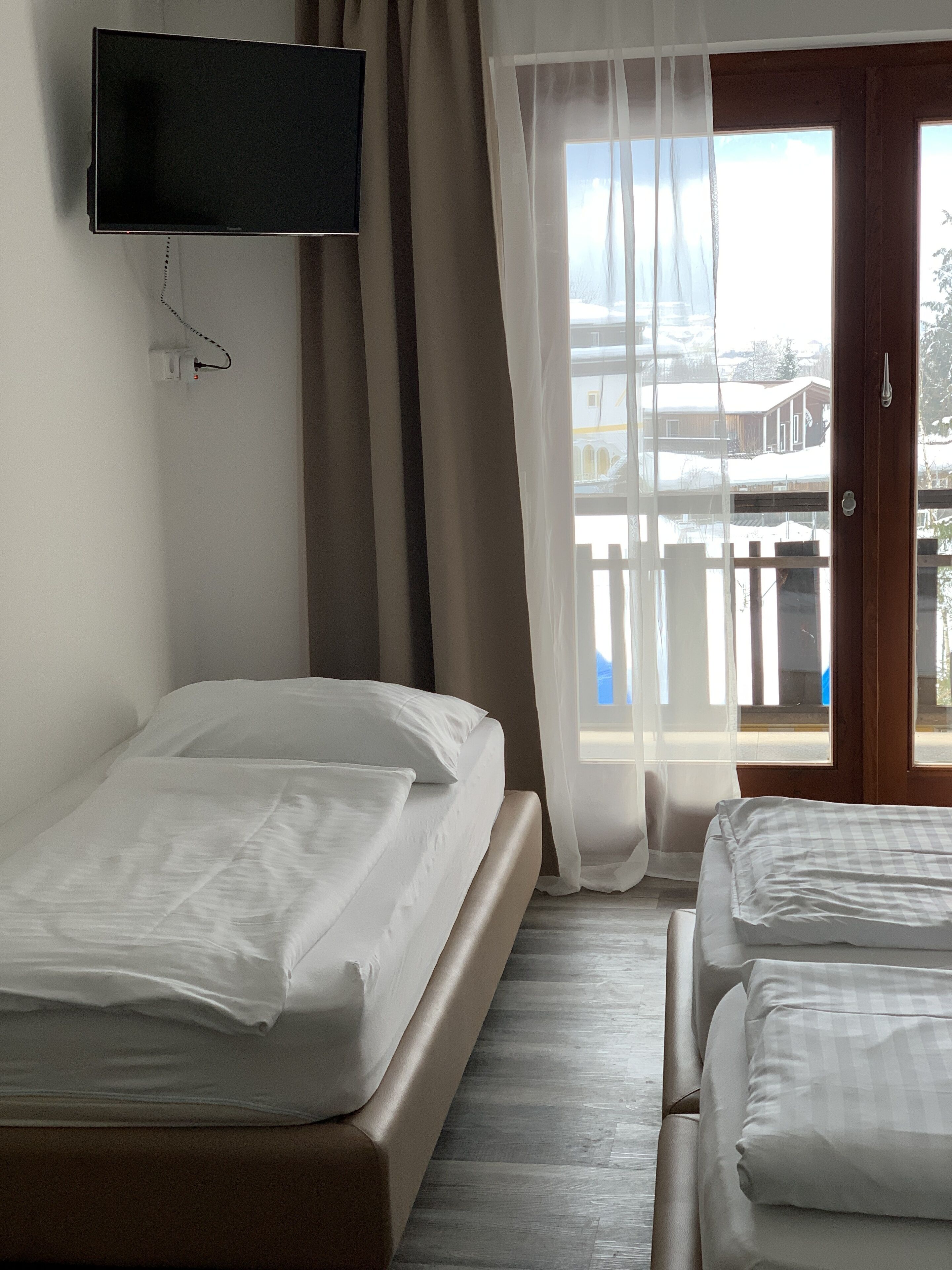 Une chambre d’hôtel avec deux lits, un téléviseur fixé au mur et un balcon donnant sur des immeubles.