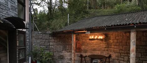 A rustic stone building with a tiled roof, a wooden table, and potted plants.