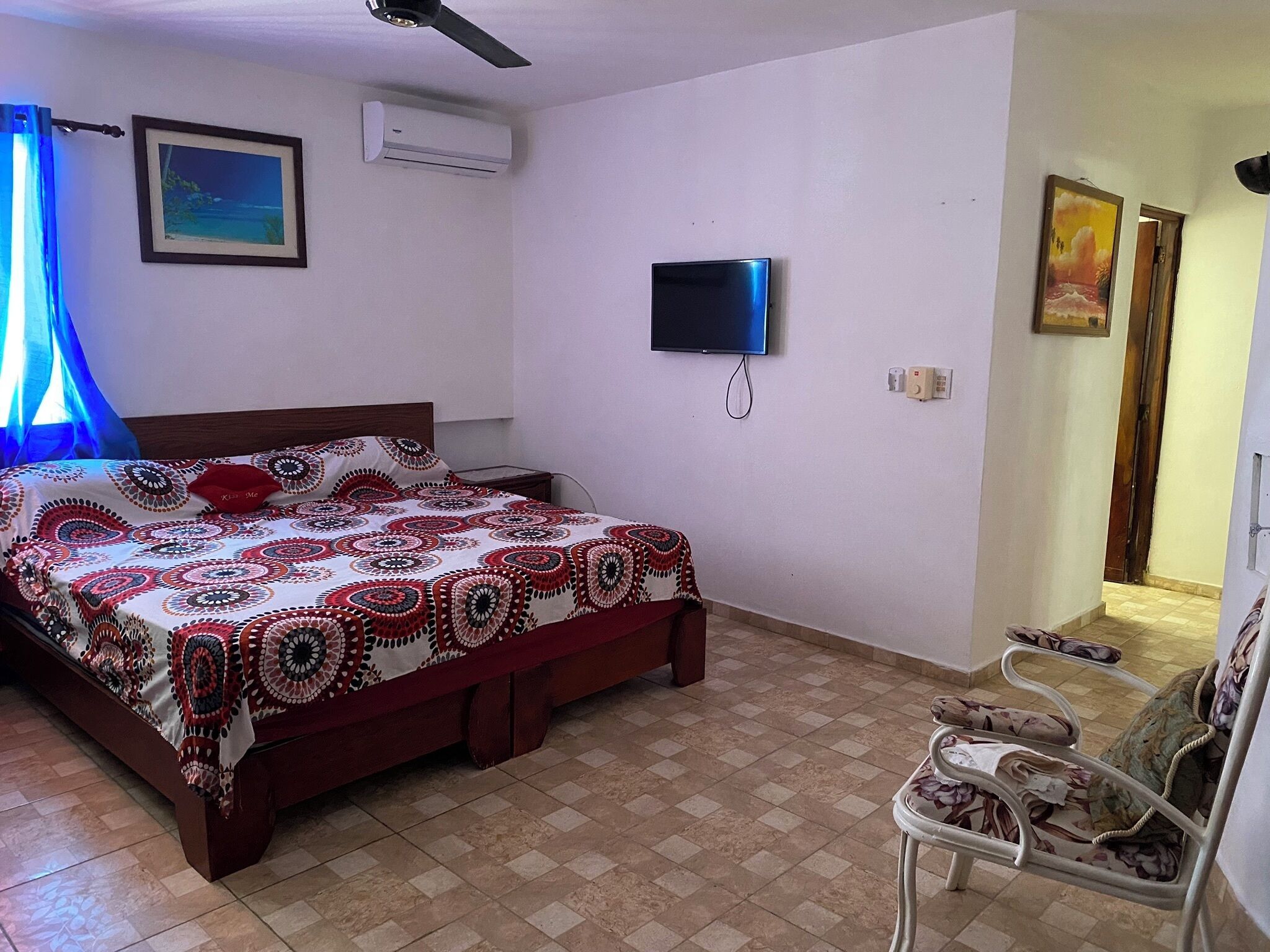A bedroom with a bed, a TV, an air conditioner, and a chair.