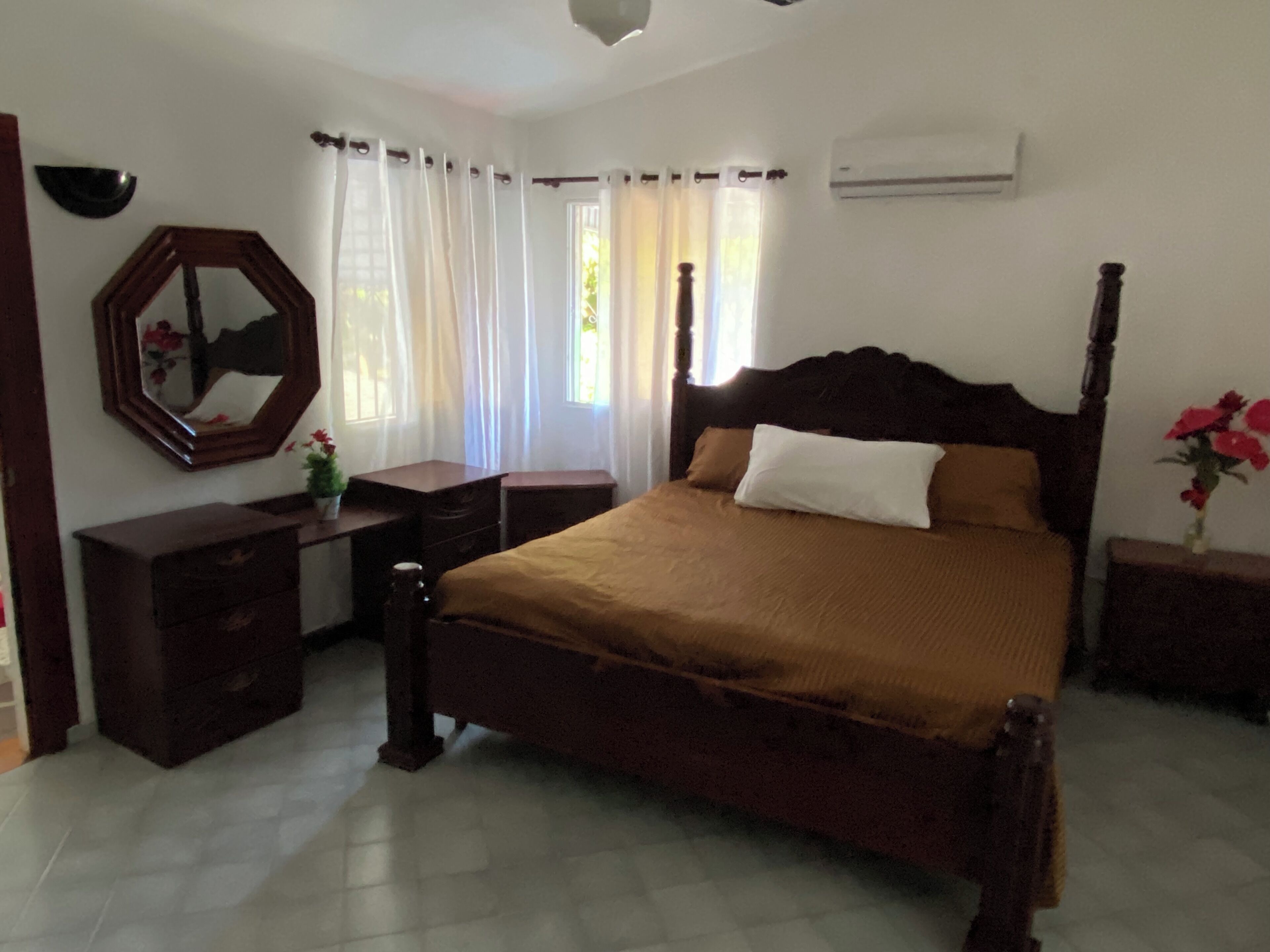 A bedroom with a wooden bed, a dresser, a mirror, and a window with curtains.