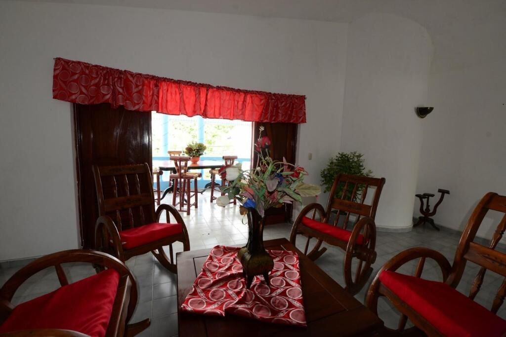 A dining area with wooden chairs and a table, red curtains, and a view of the outdoors.