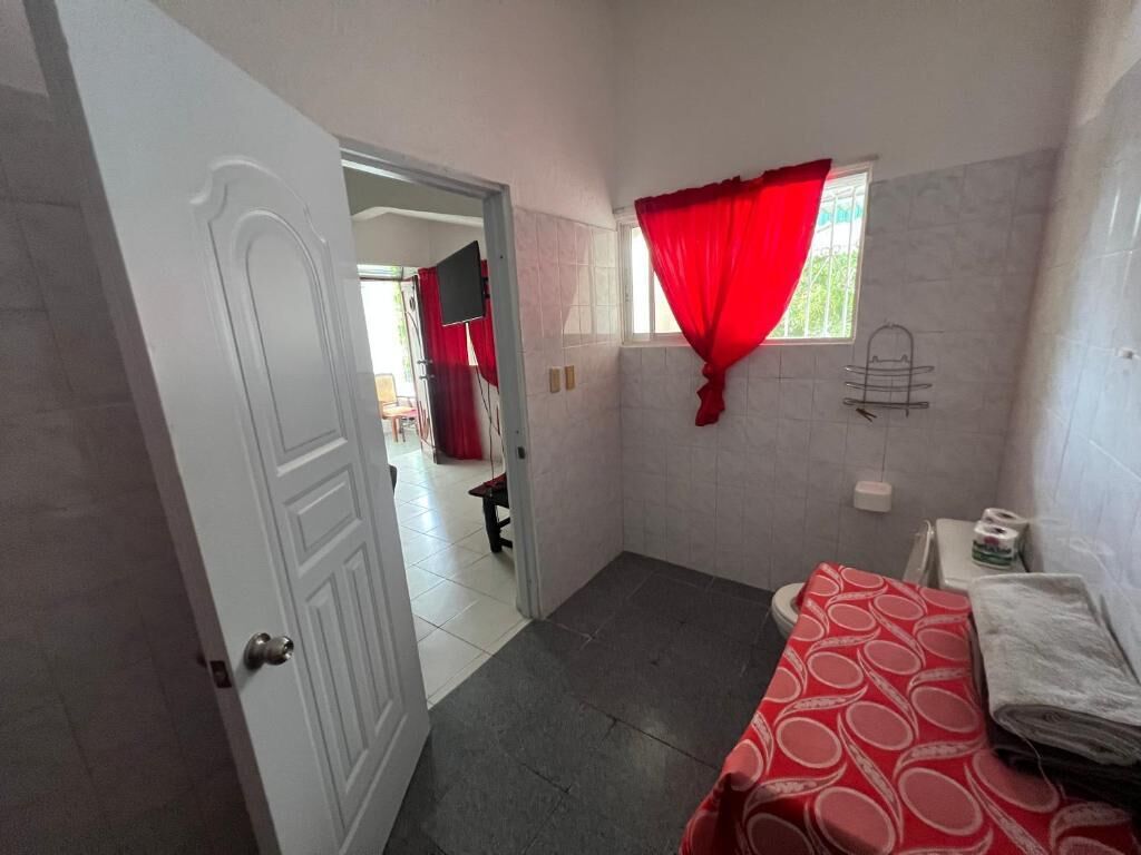 Un baño con inodoro, lavabo, espejo y ventana con cortinas rojas.