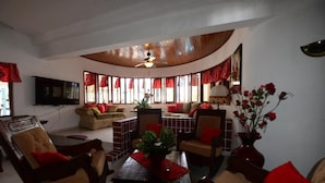 A cozy living room with a curved ceiling, a television mounted on the wall, and a dining area with a table and chairs. - Villa Antonia 16 (Sosúa)