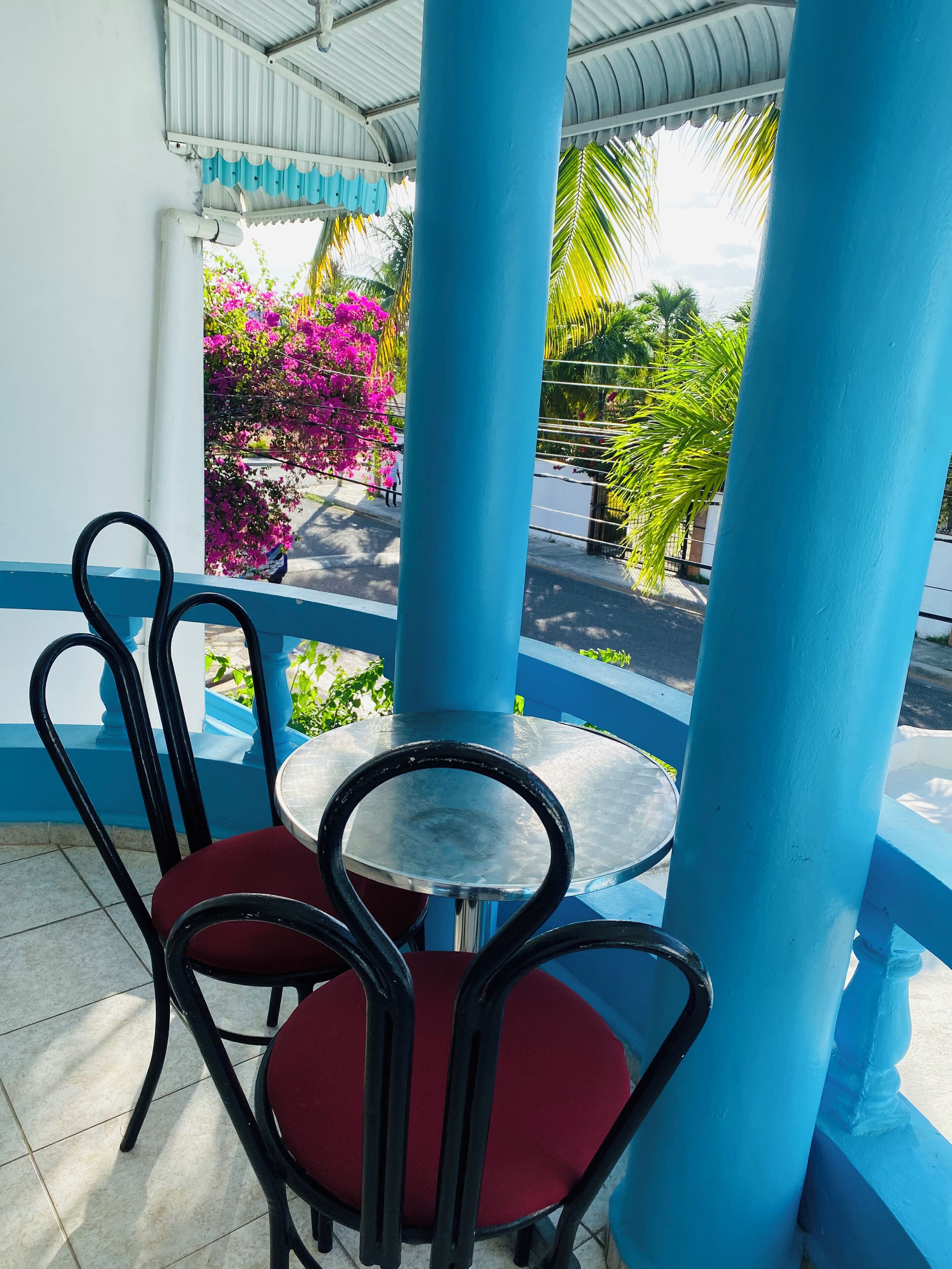 Een overdekt terras met blauwe kolommen, een ronde tafel en rode stoelen.