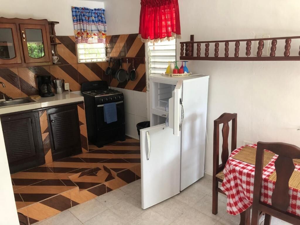 A kitchen with a stove, sink, and refrigerator, a window with curtains, and a patterned floor.