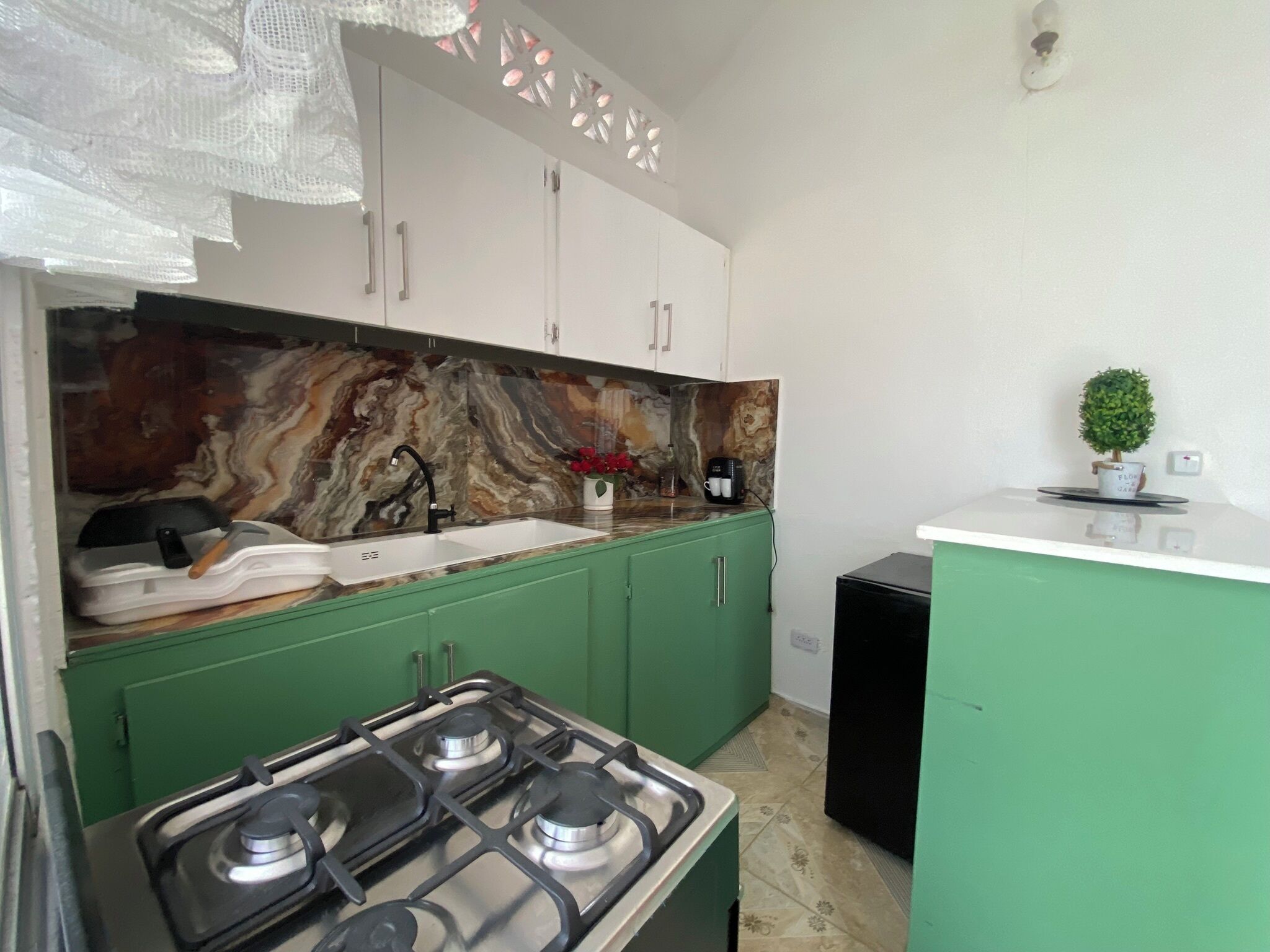 A kitchen with green cabinets, a marble backsplash, a gas stove, and a coffee maker.